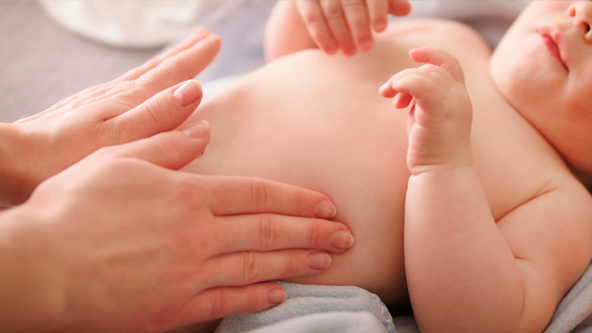 Mamá sostiene a su bebé mientras realiza ejercicios suaves para aliviar cólicos y gases durante un momento de cuidado.
