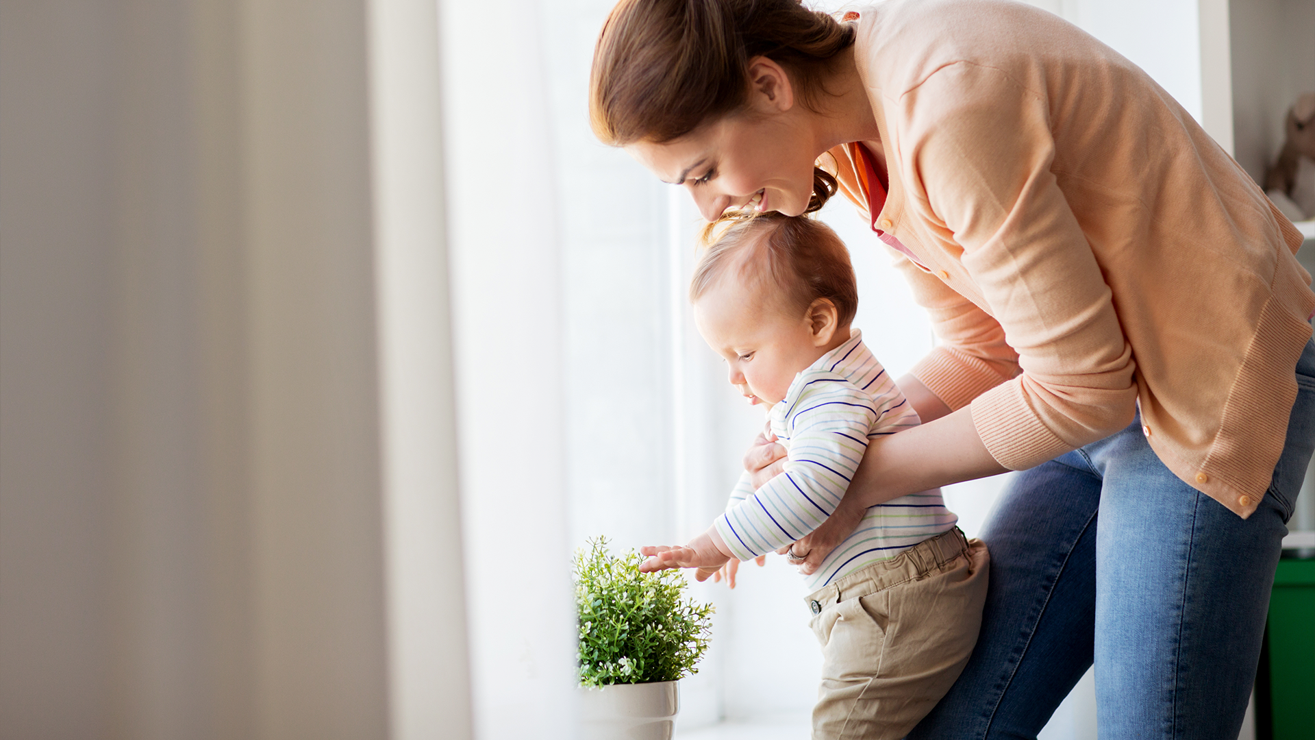 Mamá con su bebé regando plantas juntas en casa, como parte de una crianza consciente